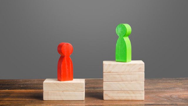 On a table, a pile of blocks (as if it were dominoes) of different heights and two dolls on top - representing the votes of different candidates