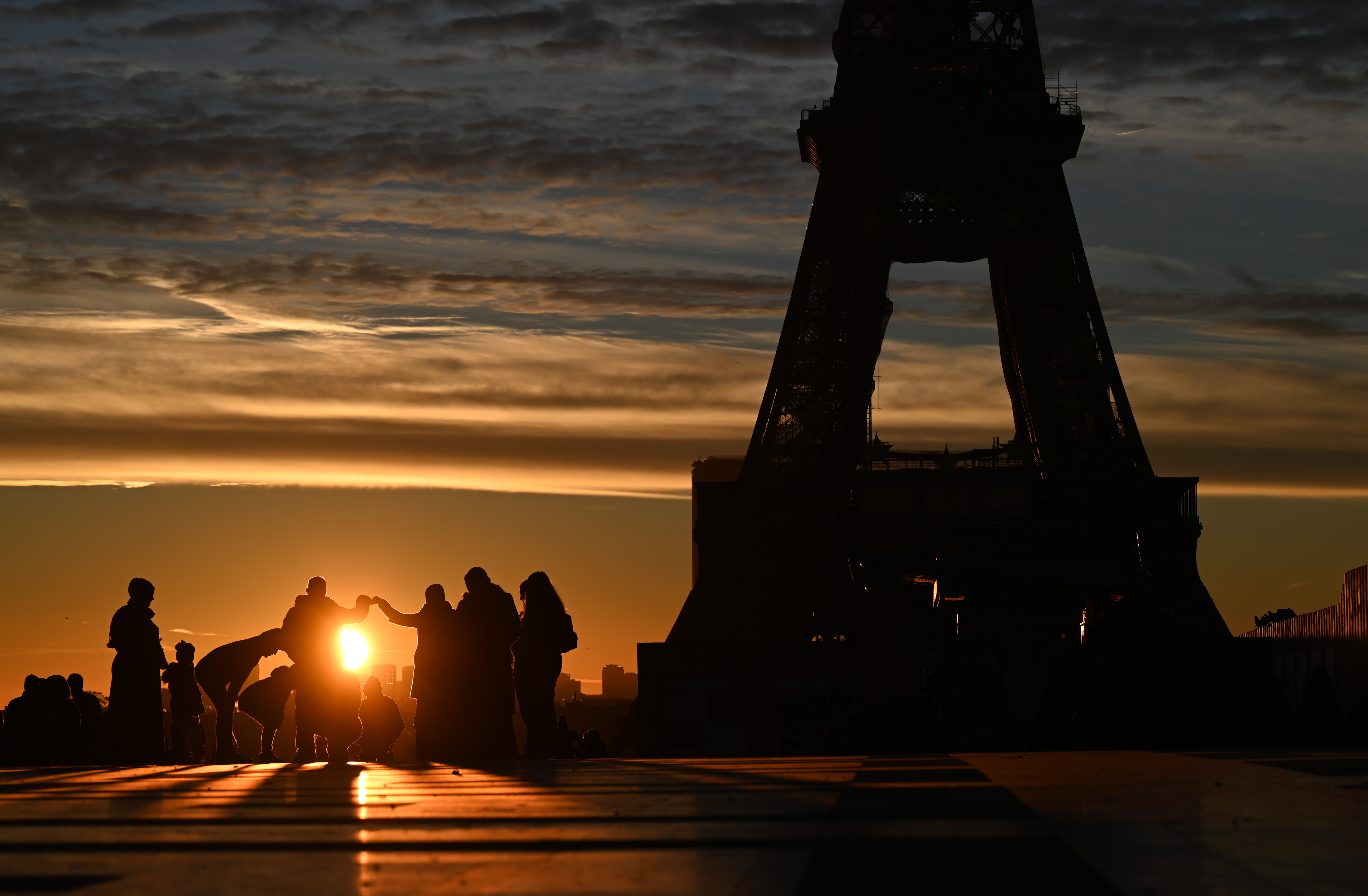 Tourists watch the sunrise near the Eiffel Tower on January 1, 2022