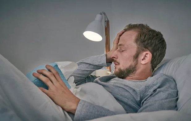 In the color photo, a man is lying on a bed with his hands on his head.