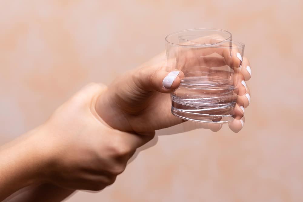 A woman with Parkinson's disease holds a glass of water